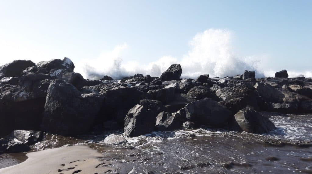 big waves hitting the wave breaker in front of the volcanic black sand on Playa de Troya