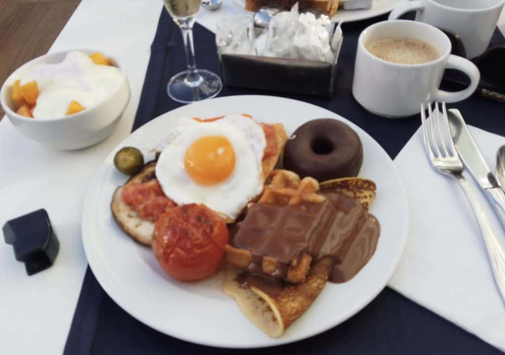 the breakfast buffet at the mediterranean palace. In the photo there is a fried egg, waffles, pancakes, a doughnut, a fried tomato, a cup of coffe and some dessert